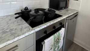 Keittiössä on valkoisilla laatoilla verhoiltu seinäosa, musta mikroaaltouuni, liesi, jossa on kattiloita, ja astianpesukone.