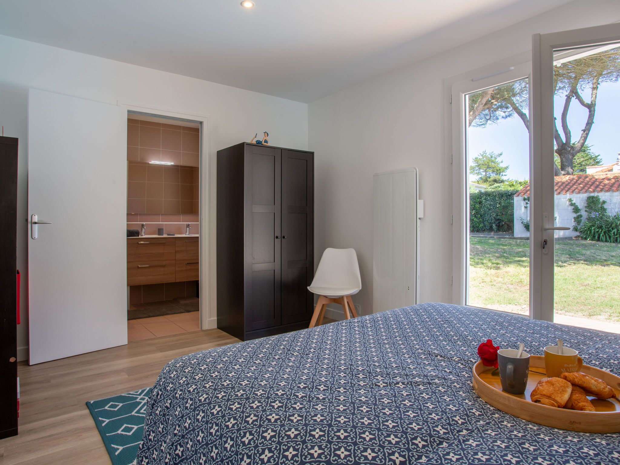 Ein Schlafzimmer mit einem Bett, einem Nachttisch mit Frühstücksgegenständen, einem Kleiderschrank und einem durch eine offene Tür einsehbaren Badezimmer.