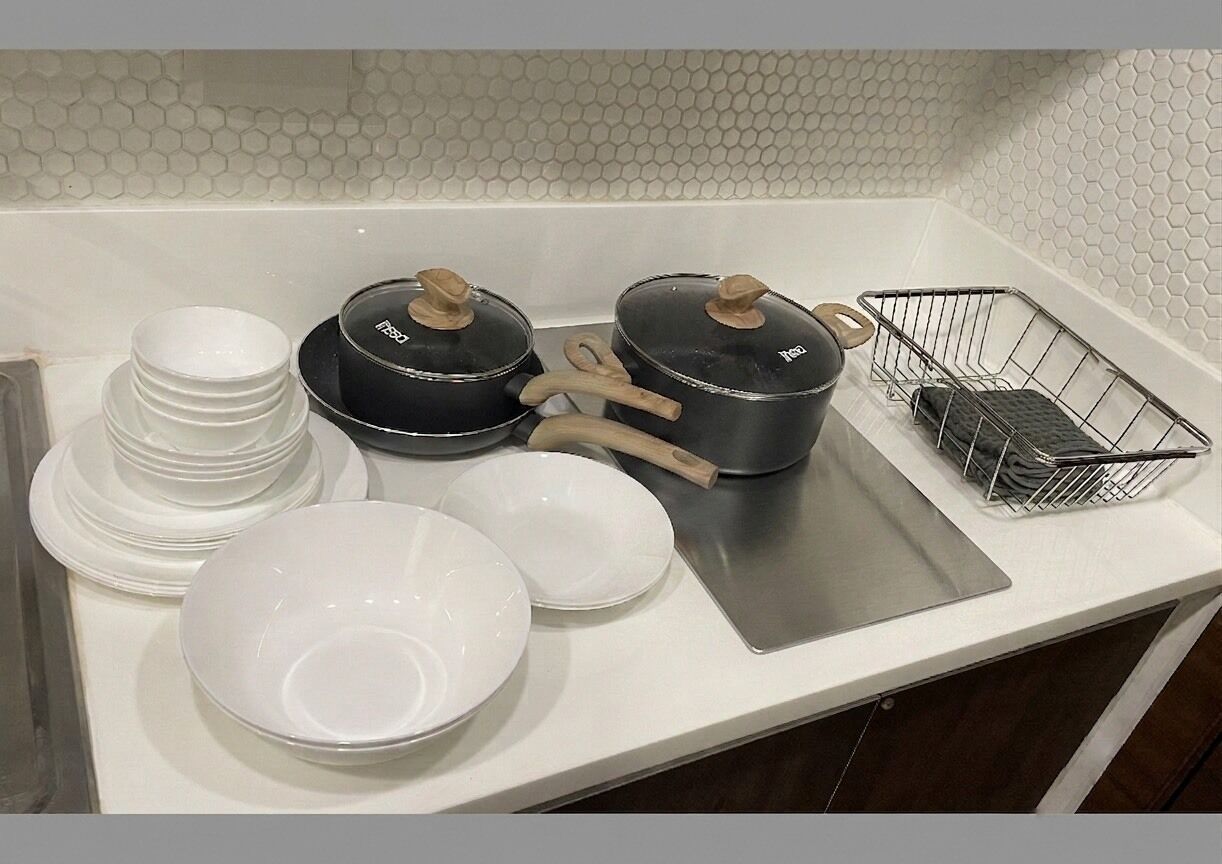 A kitchen counter with stacked white plates, two black pots with wooden handles, a metal spatula, and a wire basket.