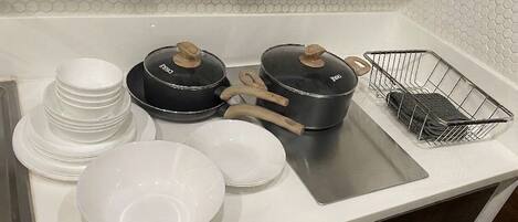 A kitchen counter with stacked white plates, two black pots with wooden handles, a metal spatula, and a wire basket.