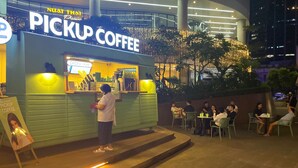 Un quiosco de café al aire libre de noche, con un letrero que dice 'PICKUP COFFEE' y una persona de pie en el mostrador.