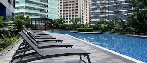 Una piscina con sillones de descanso, rodeada de vegetación y edificios modernos.