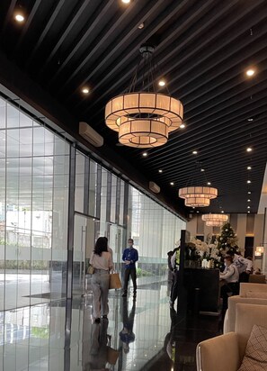 A spacious lobby with large glass windows, modern chandeliers, and a reception desk with a Christmas tree. - 1-Bedroom Condo Unit at Ayala Avenue in Makati City with Netflix Apple TV Wifi (Makati City)
