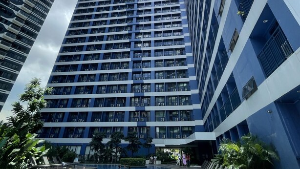 Un edificio alto con piscina en la base, rodeado de vegetación.