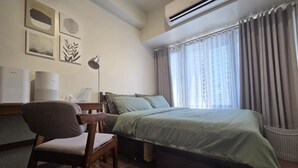 Habitación de hotel con cama, escritorio, silla, aire acondicionado y una obra de arte en la pared.