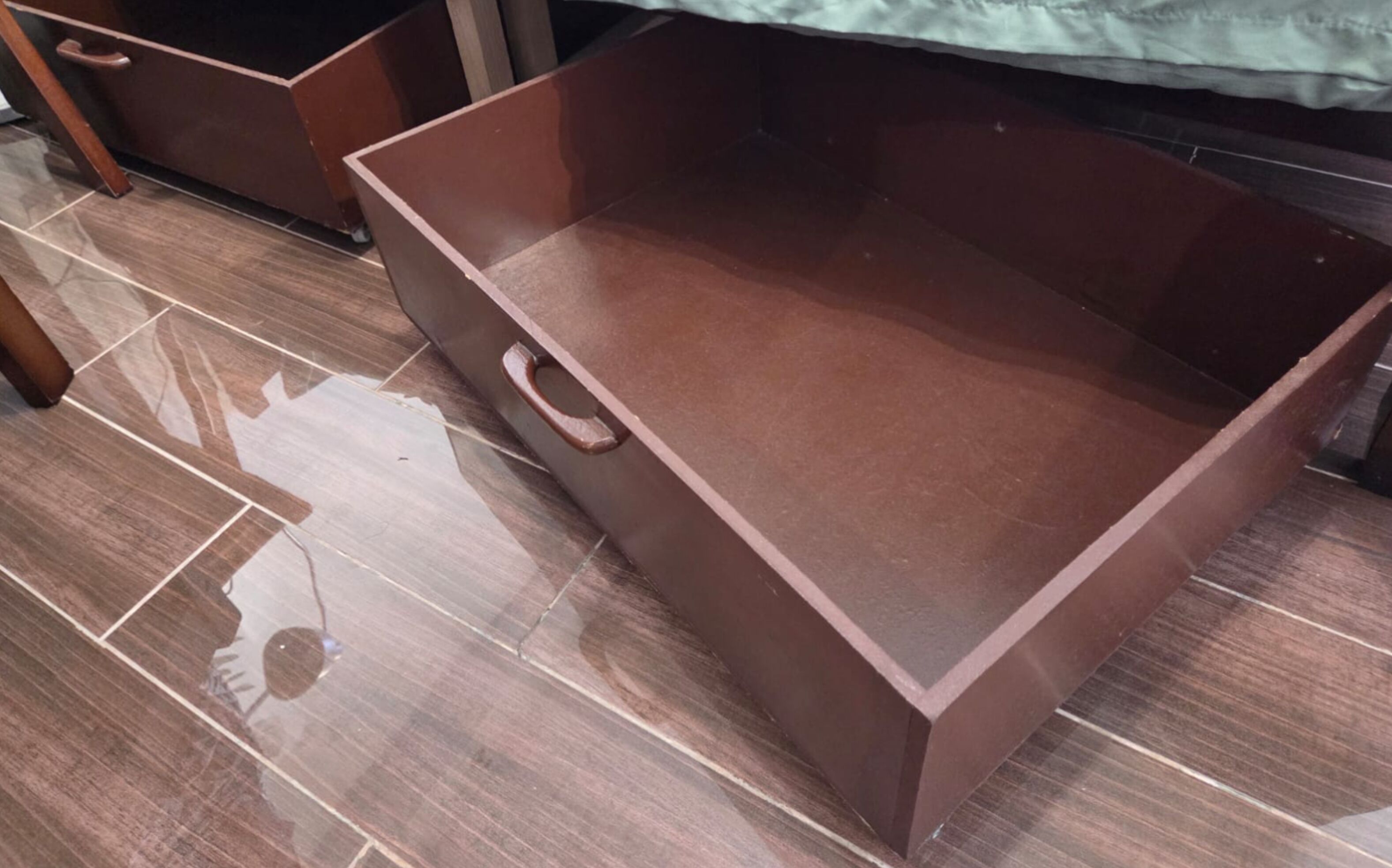 A brown, empty storage box with a handle on a tiled floor.