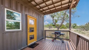 A covered porch with a wooden deck, a yellow door, and a barbecue grill. - The GlampBox. Lakefront, 20acres, Starlink Wifi! (Burnet)