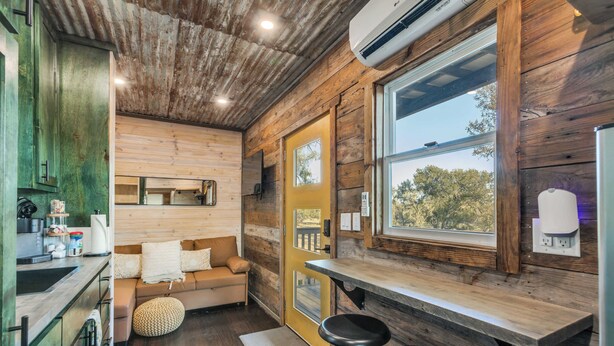A cozy cabin interior with a wooden interior, a kitchenette, a sofa, and a bar area. - The GlampBox. Lakefront, 20acres, Starlink Wifi! (Burnet)