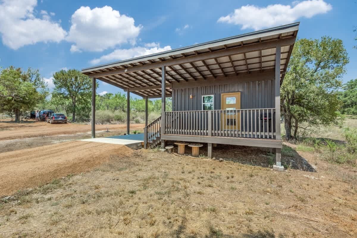 A rustic cabin with a covered porch, a small deck, and a single door.