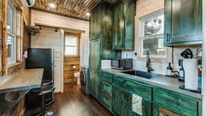 A rustic kitchen with wooden cabinets, a sink, a microwave, and a window overlooking a garden. - The GlampBox. Lakefront, 20acres, Starlink Wifi! (Burnet)
