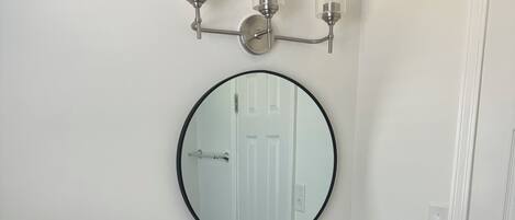 A bathroom with a white toilet, a black cabinet with a sink, a mirror, and a wall-mounted light fixture.