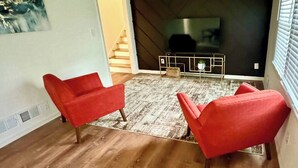 Una sala de estar moderna con un televisor grande, dos sillones rojos, un tapete estampado y una escalera que lleva a otra habitación.