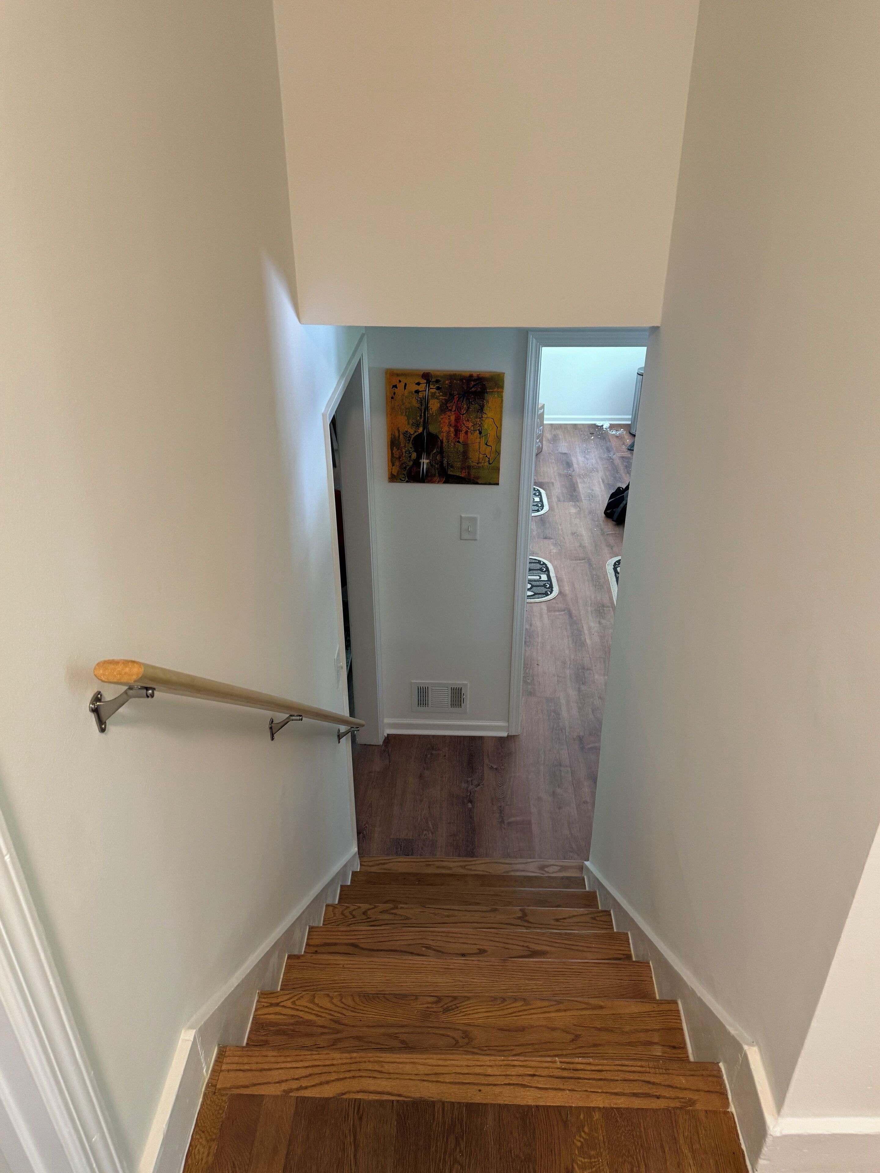 Eine Holztreppe mit Handlauf, die zu einem Raum mit einem Gemälde an der Wand führt.