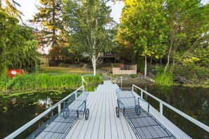 A wooden dock with metal railings and two empty chairs, leading to a house surrounded by trees and a pond with lily pads. - Starlake Villa Waterfront (Kent)