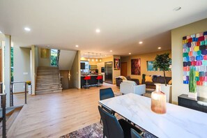 A modern kitchen with a central island, a dining area with a marble table, and a staircase leading to another level.