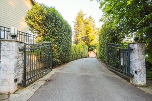 Un camino de entrada cerrado por una reja, que lleva a una casa con pilares de piedra.