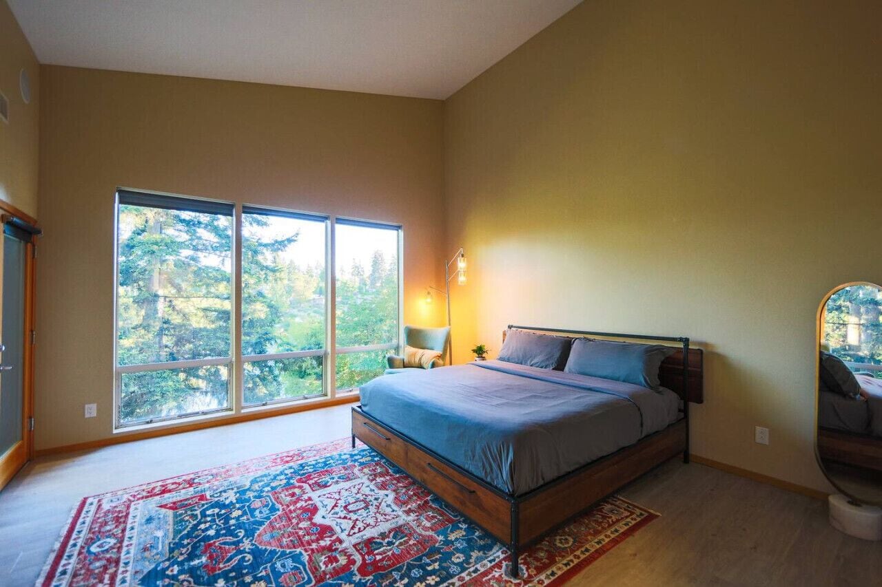 Ein Schlafzimmer mit großem Fenster, einem Bett, einem Nachttisch und einem Sessel.
