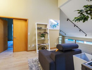 A modern living room with a grey sofa, a white shelving unit with books and a plant, and a large window with a view of the outdoors. - Starlake Villa Waterfront (Kent)