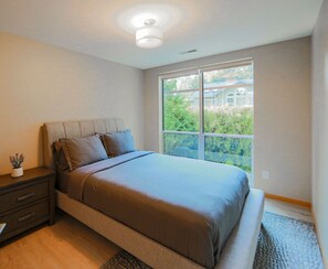 A bedroom with a large bed, a nightstand, a window with a view of greenery, and a ceiling light. - Starlake Villa Waterfront (Kent)