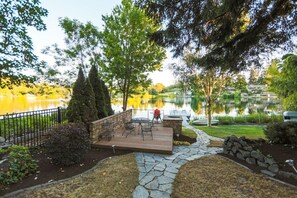 Una terraza con mobiliario exterior con vista a un lago, rodeada de árboles y un sendero de piedra.