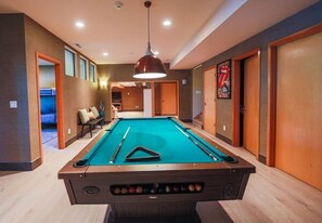 A pool table in a hotel room with a ceiling light, wooden doors, and a bench with cushions.