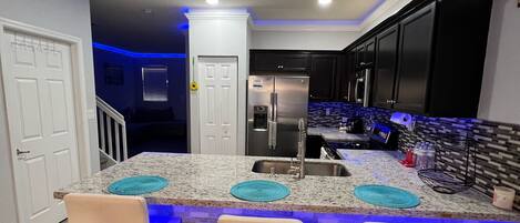 A modern kitchen with a central island, bar stools, and a built-in refrigerator.