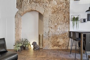 A room with a stone wall, a sofa, a dining table with chairs, and potted plants. - Apartment 'Appartamento Luxury - Torre' with Air Conditioning (Terracina)
