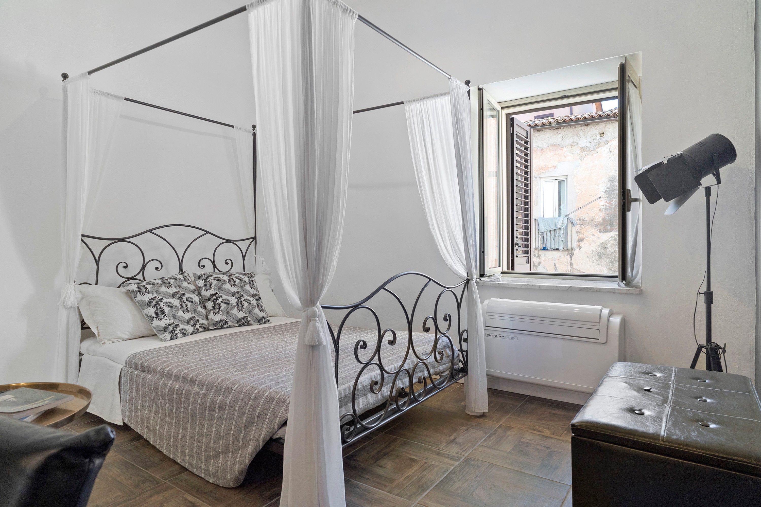 Un letto a baldacchino con tenda, una finestra vista esterna, una lampada da terra e un termosifone.