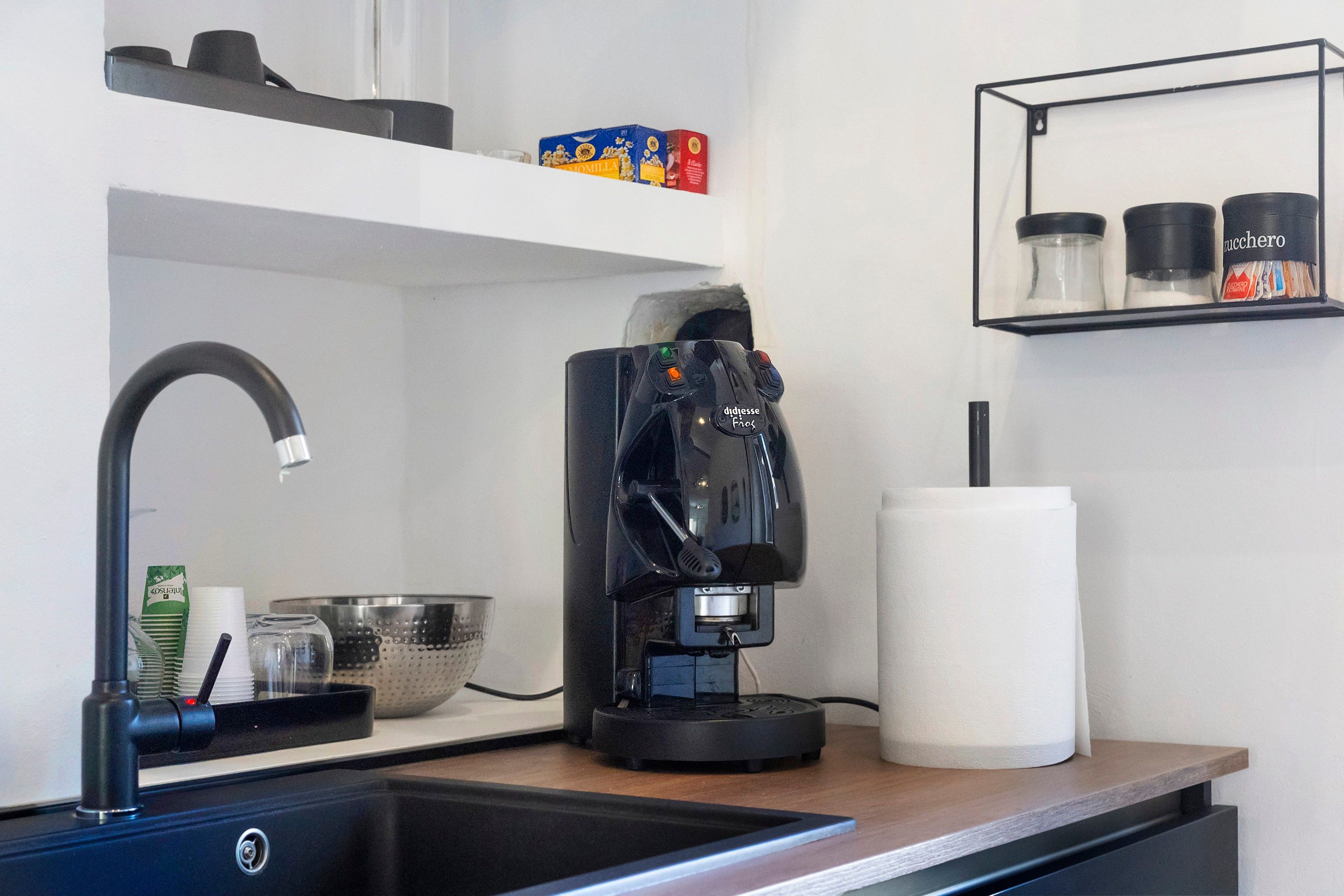 A kitchen with a coffee maker, a sink, and shelves with kitchen items.