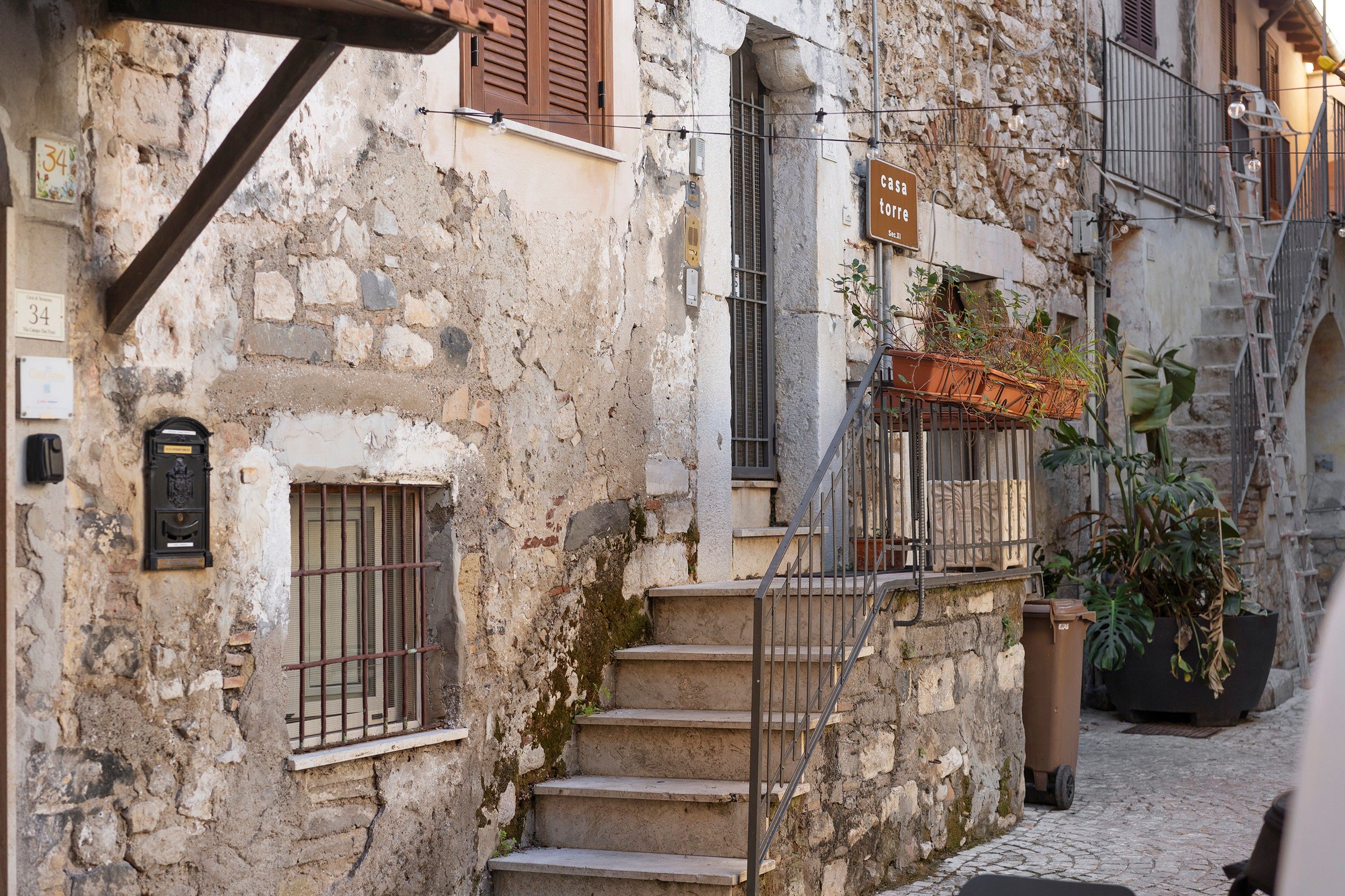 Eine schmale Gasse mit einem Steinhaus, das eine Treppe, einen Briefkasten und ein Schild mit der Aufschrift 'casa torre' zeigt.