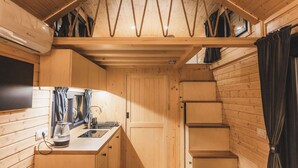 A compact wooden cabin with a kitchenette, a small window, and a staircase. - Garden Home by Tiny Away (Bessé-sur-Braye)
