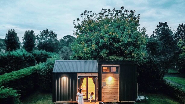 A small wooden cabin with a porch, surrounded by greenery. - Garden Home by Tiny Away (Bessé-sur-Braye)
