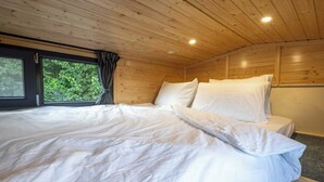 A wooden cabin bedroom with a large bed, a window with curtains, and a ceiling light. - Garden Home by Tiny Away (Bessé-sur-Braye)
