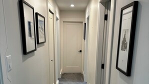 A narrow hallway with carpeted floors, white walls, and framed pictures on the walls. - Quiet corner on Burman (Gold River)