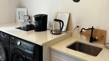 Un área de lavandería con lavadora, cafetera y pileta.