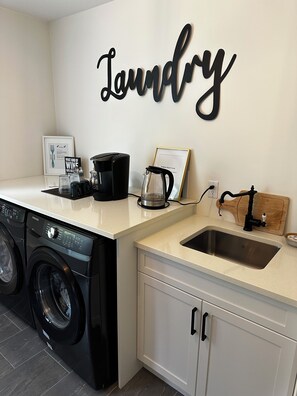Un espace buanderie équipé d’un lave-linge, d’une machine à café et d’un évier.