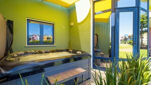 A hot tub in a room with green walls, a window, and a view of buildings outside. - Romantic flat with Jacuzzi &Pool (Albufeira)