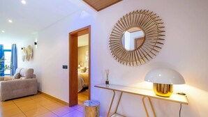 A modern living room with a sofa, a round mirror, a table with a lamp, and a trash bin. - Romantic flat with Jacuzzi &Pool (Albufeira)