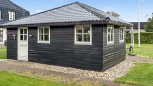 Een klein, donker houten gebouw met een pannendak, een deur en ramen.