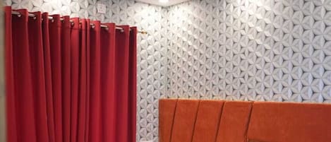 A hotel room with a bed, a nightstand, a chair, a small table, and a red curtain.