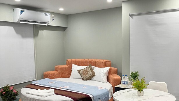 A modern hotel room with a bed, a round table, chairs, a potted plant, and an air conditioning unit. - Hotel Family Inn (Dhaka)