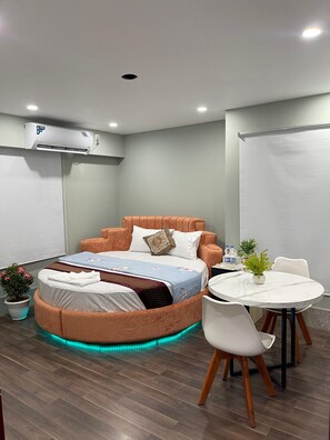 A modern hotel room with a bed, a round table, chairs, a potted plant, and an air conditioning unit. - Hotel Family Inn (Dhaka)