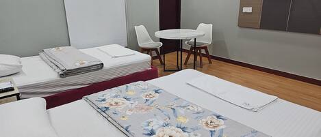 Quarto de hotel com duas camas, uma mesa pequena, duas cadeiras, uma TV fixada na parede e uma porta.