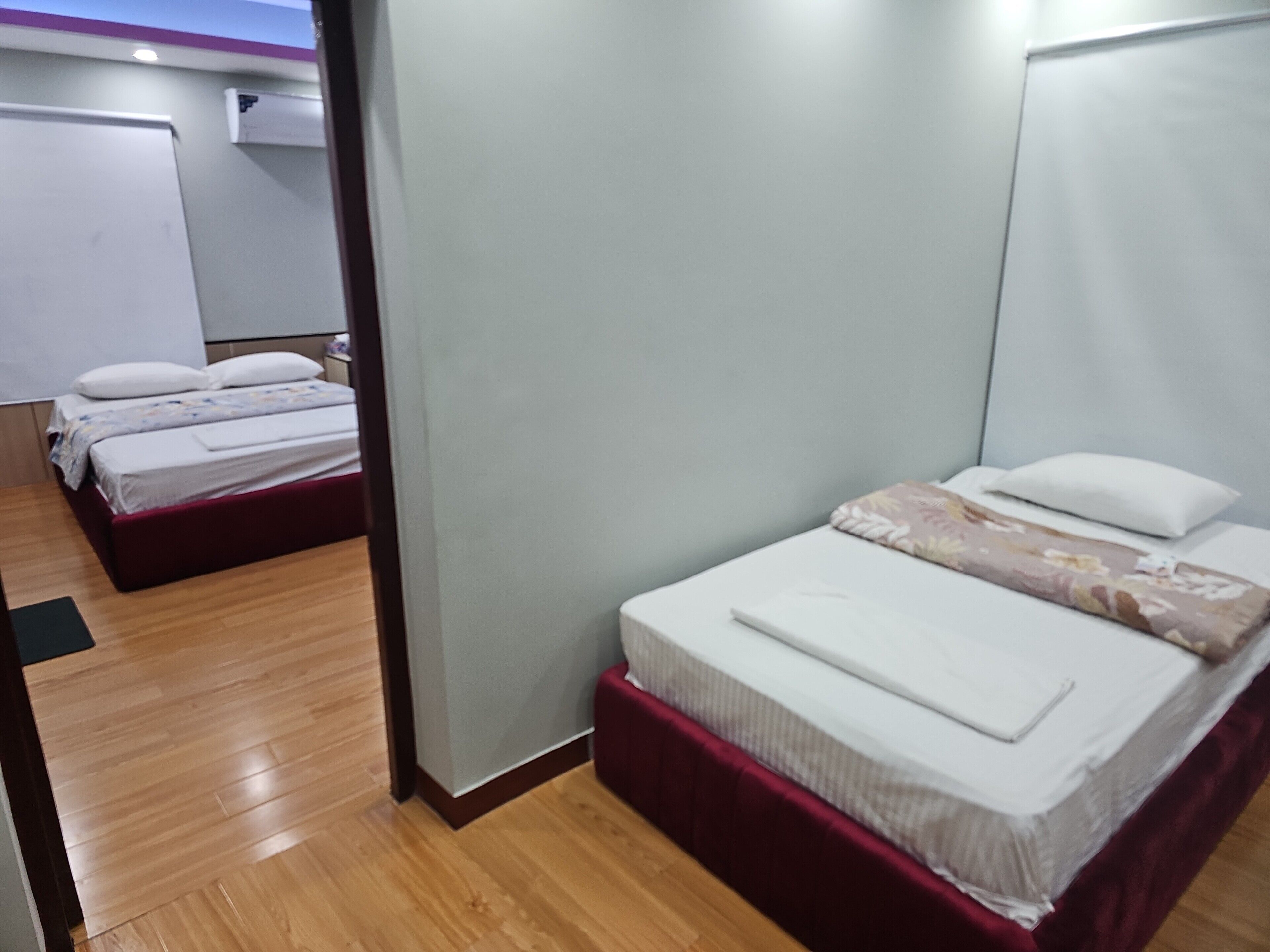 Ein Hotelzimmer mit zwei Betten, Holzboden, weißer Wand und einer Tür.