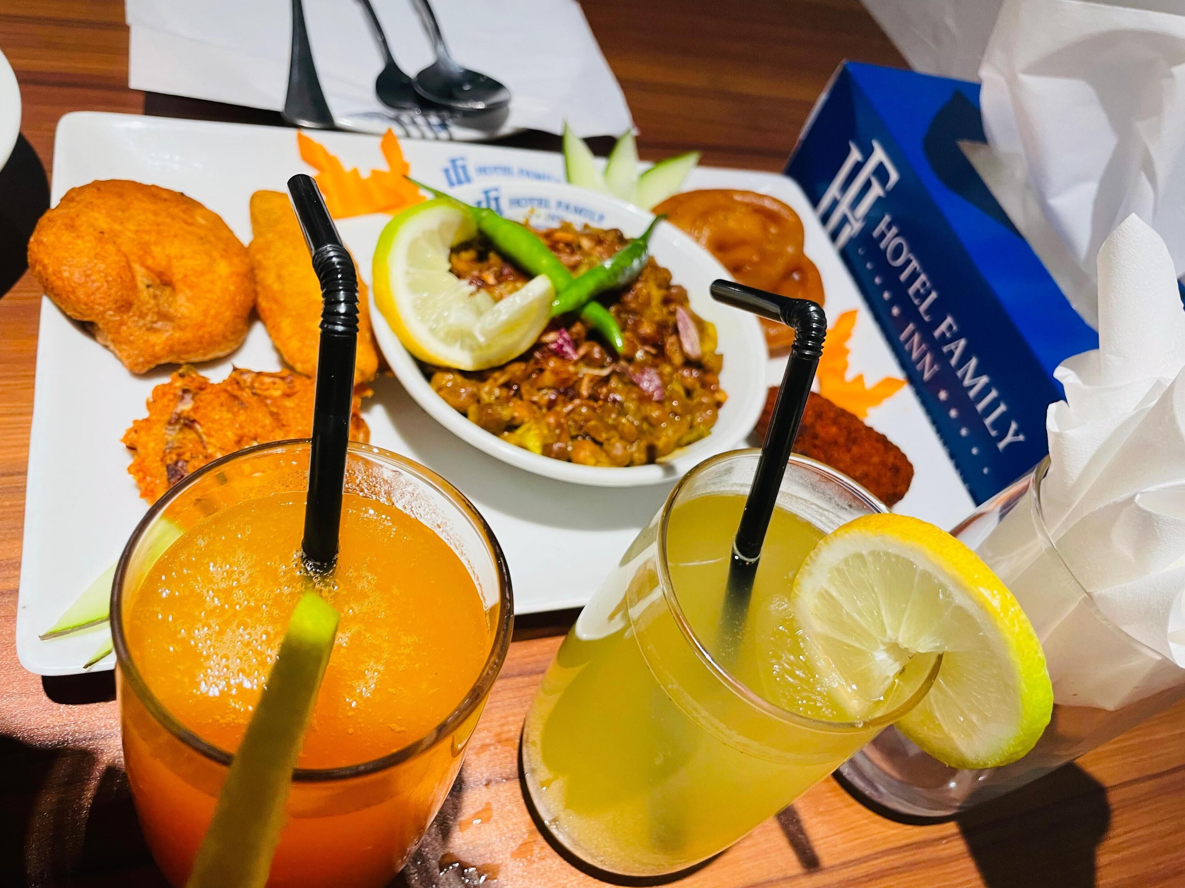 Un plato con alimentos fritos, un bol de curry y dos bebidas con rodajas de limón y pajitas.
