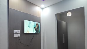 A modern room with a flat-screen TV mounted on a wall, a wooden floor, and a door with a circular window. - Hotel Family Inn (Dhaka)