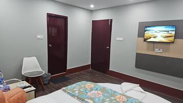 Una habitación de hotel con cama, televisor montado en la pared, dos puertas, una silla y una mesita con un control remoto.