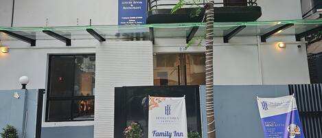 A hotel entrance with a sign indicating 'Hotel Family Luxury Room & Restaurant' and a banner stating 'Family Inn Restaurant Open for all'.