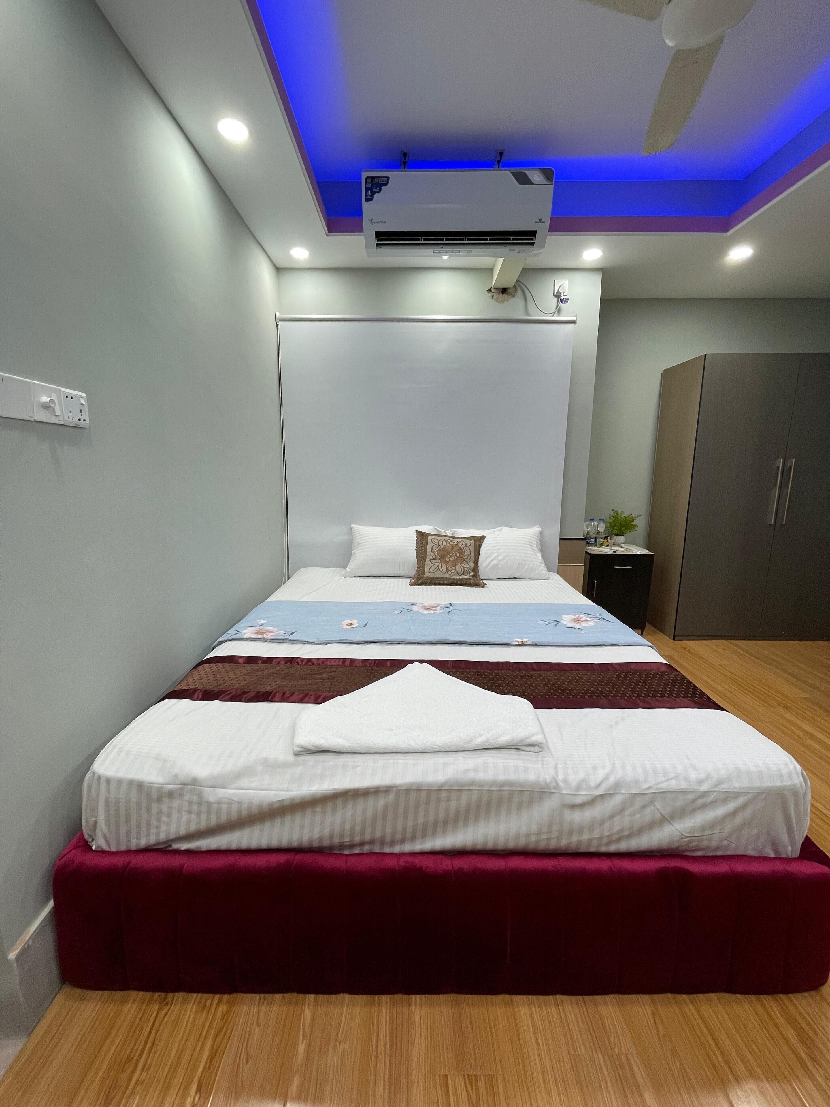 A modern hotel room with a large bed, a ceiling fan, an air conditioning unit, and a wardrobe.