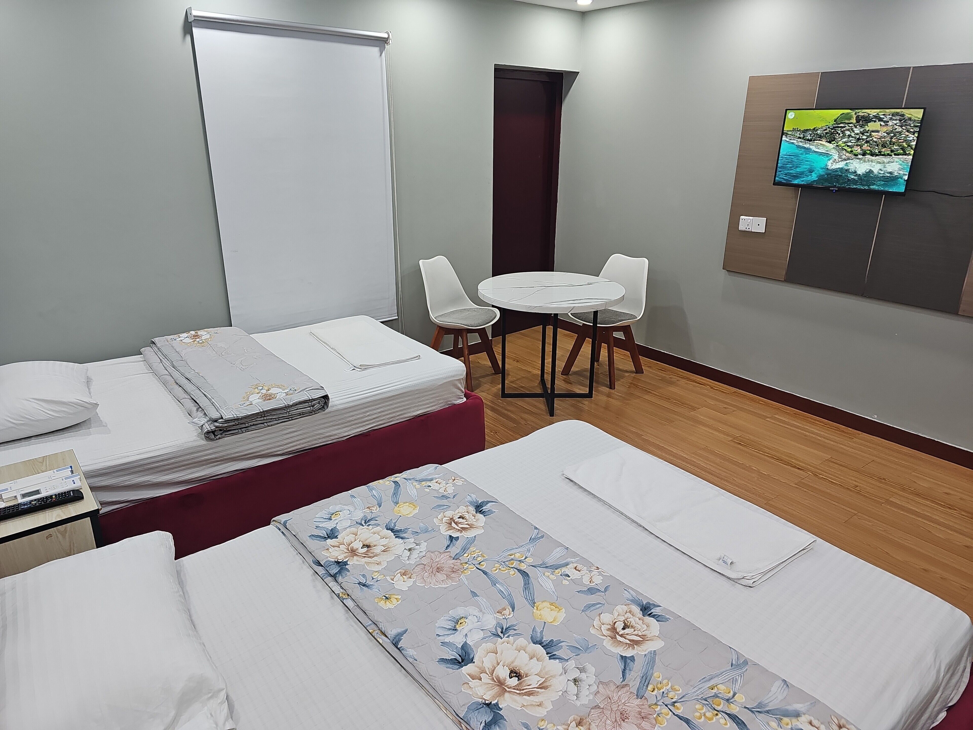 A hotel room with a bed, a desk, a chair, a small table, and a TV mounted on the wall.